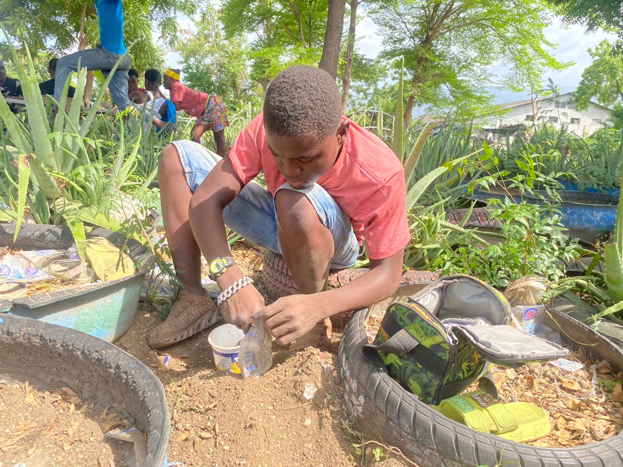 Young man working in the Jaden Tap Tap community garden, surrounded by plants and recycled tire planters